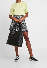 Jasnożółta koszulka z krótkim rękawem, spódnica w czarno-białe wzory, czarna pleciona torba na ramię oraz czarne trampki z białą podeszwą.