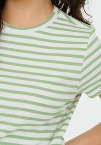Grøn- og hvidstribet ribbet t-shirt med rund halsudskæring og korte ærmer, der har vandrette linjer i varierende bredder. Blød tekstur.