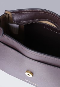 Borsa in pelle marrone con texture, dotata di chiusura con zip e accentuazione metallica dorata. L'interno presenta una fodera chiara per una migliore visibilità.