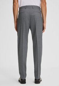 Graue, strukturierte Anzughose mit maßgeschneiderter Passform, die zwei Gesäßtaschen und ein einzelnes Biesen-Design aufweist, getragen mit schwarzen Schuhen.
