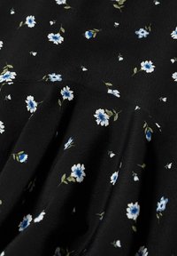 Tessuto nero con motivo floreale bianco e blu, caratterizzato da fiori delicati e foglie verdi, superficie strutturata con un morbido drappeggio.