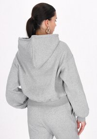 Felpa corta grigia realizzata in tessuto morbido, con cappuccio, polsini a coste e orlo elastico. Il design è semplice e privo di motivi rilevanti.