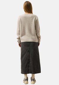 Maglione grigio a coste abbinato a una lunga gonna di jeans nera, indossato con calzini crema e sneakers beige. Stile semplice e funzionale.