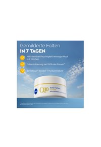 White round jar with a yellow band and blue text, promoting anti-wrinkle cream. Soft blue background with clouds. Text in German.