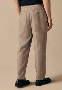 Pantalones a rayas marrones con una tela texturizada, que presentan un corte relajado, dos bolsillos traseros y combinados con zapatos negros.