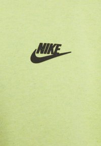 T-shirt en coton vert clair avec un logo "NIKE" noir et un swoosh. Le tissu a une texture lisse avec un léger éclat.