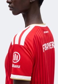 Personne portant un maillot de sport rayé rouge et blanc avec « FBAYER » et le logo Allianz sur la manche, vue de côté et de dos.