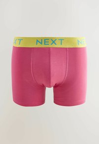 Rožiniai medvilniniai boxer šortai su geltonu juosmeniu, kuriame yra mėlynas "NEXT" logotipas. Lygus tekstūra, prigludęs dizainas ir vidutinio ilgio iki šlaunų.