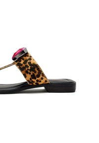 Sandalia plana de estampado de leopardo con una tira ancha, adornada con una gran gema rosa y una suela negra. Material texturizado con un acabado suave.