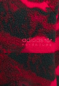 Červená a černá fleecová tkanina s texturovaným povrchem, s logem "adidas ADVENTURE" v odpovídaj�ící červené výšivce.