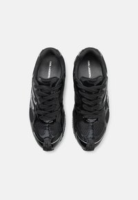 Baskets de sport noires avec une finition brillante en vernis et des détails en maille. Dotées de lacets noirs et de semelles en caoutchouc texturées distinctives.