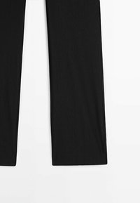 Pantalon noir à jambes droites étalé à plat sur une surface blanche, montrant la moitié inférieure des deux jambes du pantalon.