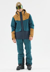 Teal and brown two-tone snow jacket with a hood, zippers, and elastic cuffs paired with matching teal snow pants and black boot accents.