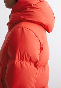 Czerwona kurtka puchowa z kapturem, pikowany design oraz błyszczące wykończenie. Posiada logo w pobliżu suwaka po boku.