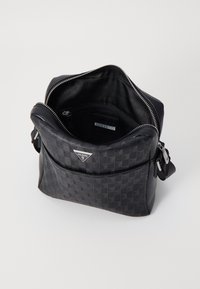 Bolso de mano sintético negro con patrón geométrico en relieve. Cuenta con cierre de cremallera, bolsillo frontal y placa de logo de la marca. Textura suave.