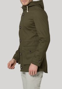 Veste à capuche vert olive avec fermeture à boutons, deux poches avant et poignets élastiques. Fabriquée en tissu robuste, avec cordons de serrage à la capuche.