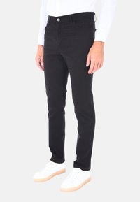 Pantaloni neri in cotone con vestibilità slim, dotati di chiusura a bottone, cinque tasche e una texture liscia. Abbinati a sneakers bianche.