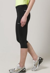 Pantaloni capri atletici neri in materiale elasticizzato, con fascia in vita alta. Abbinati a scarpe da corsa argento con suole nere e dettagli dorati.