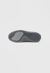 Zool van een grijze Vans-schoen die het wafelpatroon van de loopzool laat zien, met een lichter getextureerd gebied bij de bal van de voet tegen een witte achtergrond.