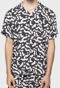 Camicia a maniche corte in tessuto blu navy con un motivo astratto bianco, con chiusura a bottoni e taschino a toppa sul lato sinistro.