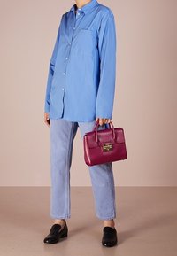 Ljusblå långärmad skjorta, raka ljusa jeans, svarta loafers, håller en mörkrosa handväska med guld detaljer.