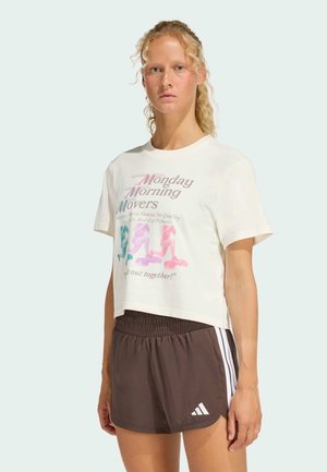 White cropped t-shirt with colorful graphic print, paired with dark brown athletic shorts featuring white stripes and logo on the side.