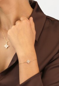 Gold bracelet with a floral charm featuring circular crystal accents, worn on a wrist, complemented by a matching pendant necklace.