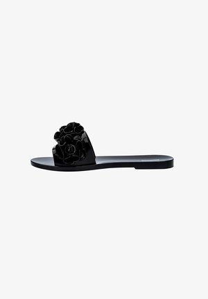 Black slide sandal with a glossy finish, featuring a large floral decoration on the strap and a flat sole. Simple and modern design.
