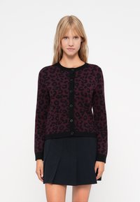 Leopard print cardigan in dark burgundy and black, featuring a round neck, button closure, and ribbed cuffs and hem. Worn with a dark skirt.