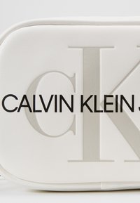 Bustina in pelle bianca con logo "CALVIN KLEIN" in rilievo e texture liscia; presenta una forma rettangolare elegante con bordi arrotondati.