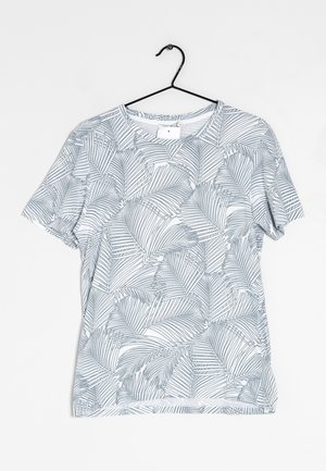 Hvid T-shirt med korte ærmer og gråt palmeblads mønster, hængende på en sort metalbøjle mod en hvid baggrund.