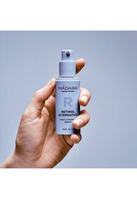 Ljuslila pumpflaska märkt "MÁDARA Retinolalternativ Växtbaserat Serum," i storlek 30 ml, hålls i en hand mot en neutral bakgrund.