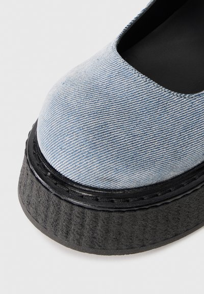 Κοντινό πλάνο από ένα ανοιχτό μπλε ριγέ υφασμάτινο επάνω μέρος παπουτσιού με παχύ μαύρο υφασμένο πέλμα και μαύρη εσωτερική επένδυση.