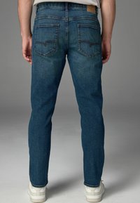 Jeanși din denim albastru închis, cu o croială slim, având două buzunare la spate, o etichetă din piele pe talie și o croială dreaptă.