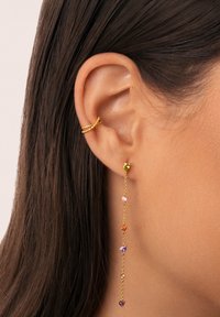 Pendientes de oro con acentos de piedras preciosas de colores en diversas formas, colgando delicadamente del lóbulo con un diseño minimalista.