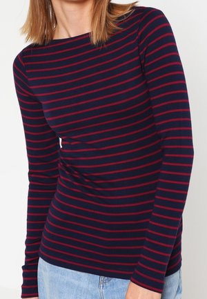 Marineblaues Langarmshirt mit roten horizontalen Streifen, Rundhalsausschnitt, tailliertem Schnitt und weicher Stoffstruktur. Kombiniert mit Denim.