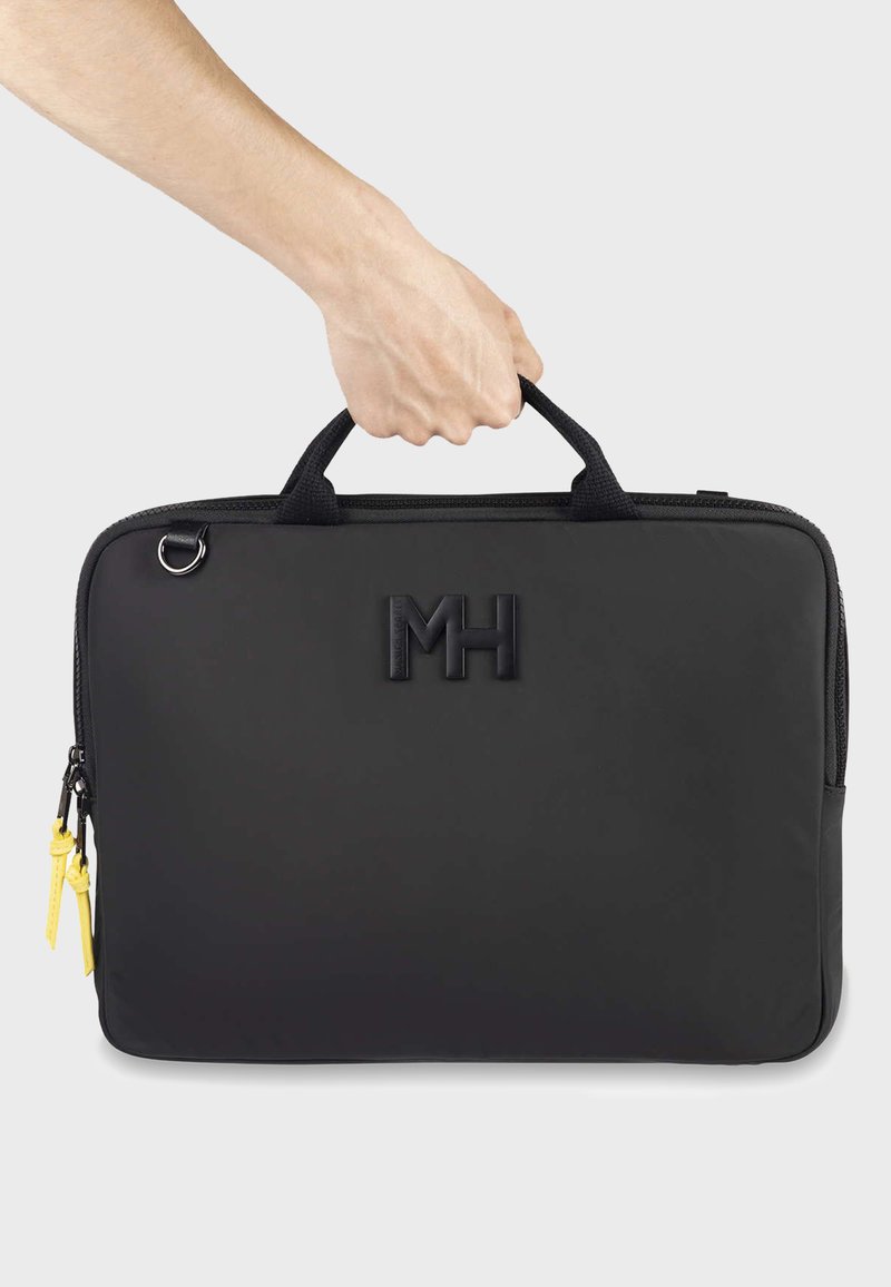Sac d'ordinateur portable noir en matériau lisse, doté de deux poignées, d'un logo "MH" embossé, d'un curseur de fermeture éclair jaune, et d'une forme rectangulaire structurée.