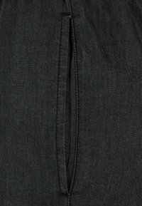 Black fabric garment featuring a vertical slit with a clean seam, made from a textured material, providing a subtle contrast to the surface.