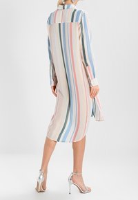Robe chemise rayée dans des couleurs pastel légères, avec des lignes verticales, dotée d'un col, de manches longues et d'une coupe mi-genoux. Talons argentés.