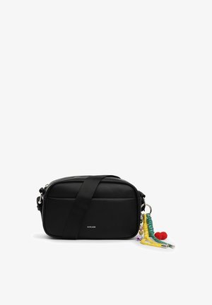 Sac bandoulière rectangulaire noir avec une sangle large et un porte-clés coloré orné d'un pompon rouge sur un fond blanc.