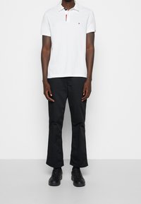 Polo blanc avec un col noir et des accents rouges, associé à un pantalon noir et des chaussures noires. Design simple avec des manches courtes.