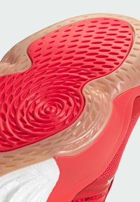 Red sole with textured pattern in circular and hexagonal shapes, transitioning to a tan rubber edge; sides feature breathable red mesh material.