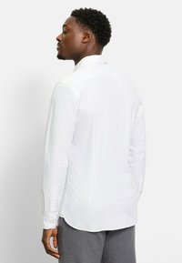 Weißes Langarmhemd mit spitzem Kragen, subtiler Textur und geknöpften Manschetten. Mit abgerundetem Saum für eine figurschmeichelnde Optik gestaltet.