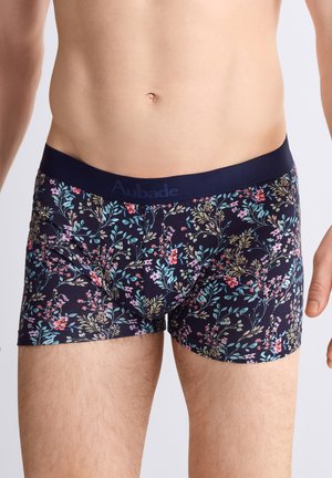 Torse masculin portant un boxer bleu marine foncé avec un motif floral multicolore et une ceinture unie bleu marine.