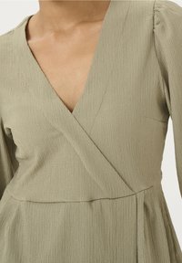 Olivgrünes Kleid aus strukturiertem Stoff mit V-Ausschnitt, langen Puffärmeln und tailliertem Schnitt mit ausgestelltem Rock.