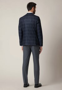 Granatowa kurtka w kratę o zdefiniowanej sylwetce, zestawiona z szarymi spodniami. Materiał ma subtelną teksturę i wiele guzików na rękawach.