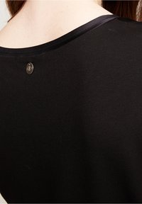 Svart tygblus med rundad halsringning och en liten metallaccent på baksidan, som framhäver den släta texturen och det enkla designen.