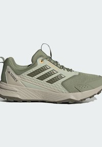 Hellgrüner Sportschuh mit strukturiertem Mesh-Obermaterial, Gummisohle und drei dunklen Streifen. Verfügt über verstärkte Ferse und orangefarbene Akzente.