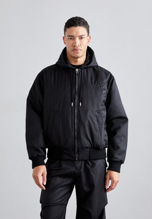 Schwarze Bomberjacke mit vertikalen Streifen, Reißverschluss vorne, Kapuze, elastischen Bündchen und Saum. Glattes, leicht glänzendes Material mit seitlichen Taschen.