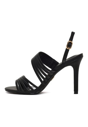 Sandalo nero con tacco alto con diverse sottili fasce sul piede e cinturino alla caviglia con fibbia dorata su sfondo bianco.